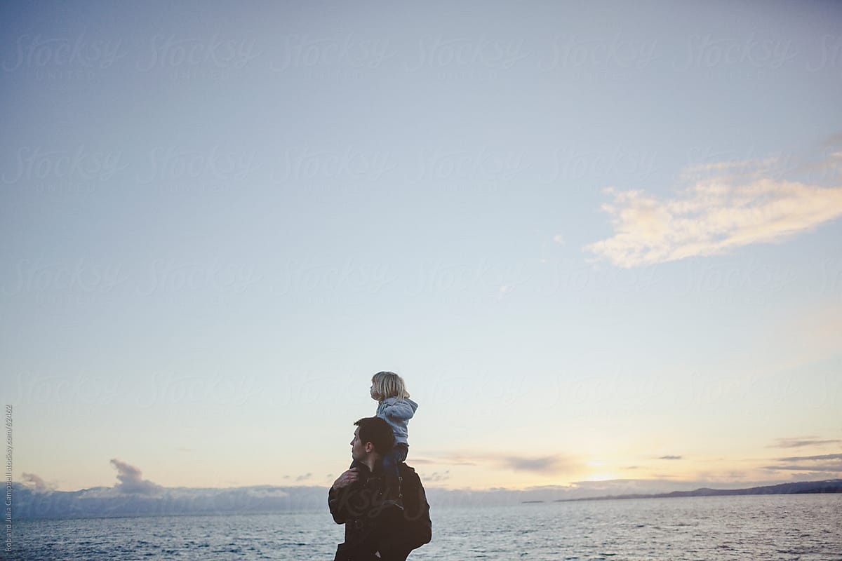 Dad gives two year old daughter shoulder ride with ocean sunset view