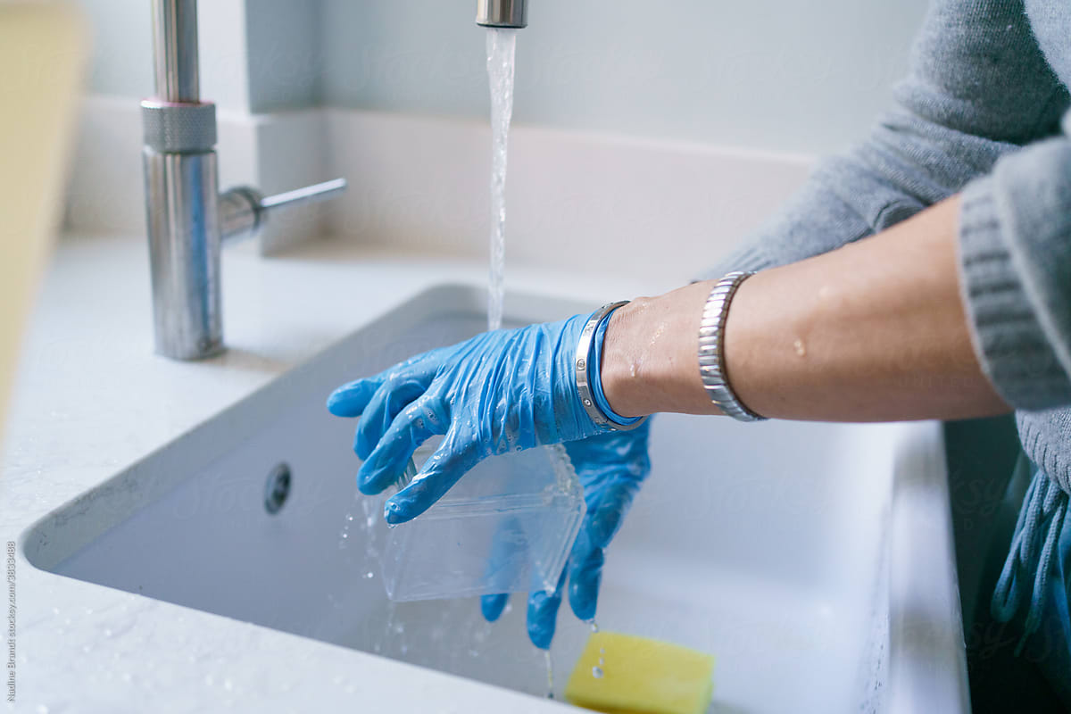 Female hands in gloves cleaning container over modern sink