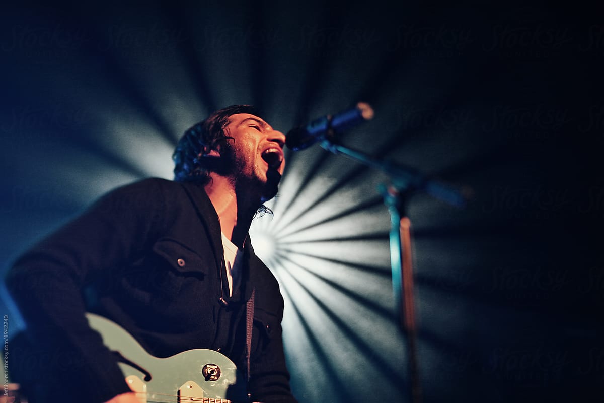 A man singing and playing guitar on stage with lights during a concert