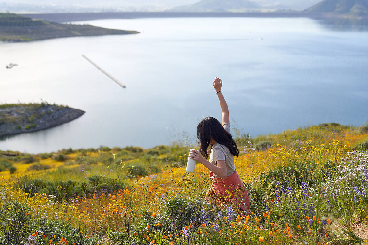 South east asian girl walks in field of flowers with lake in distance