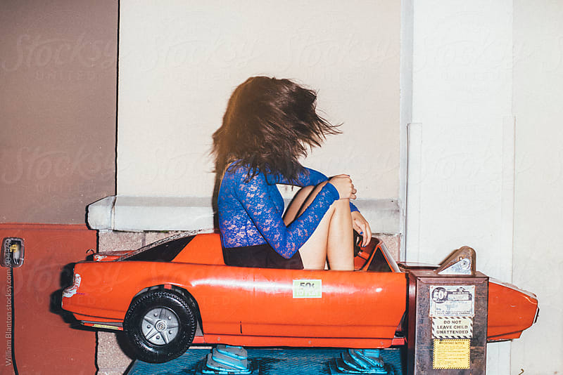 Woman fashion model posing and riding coin operated car ride at night