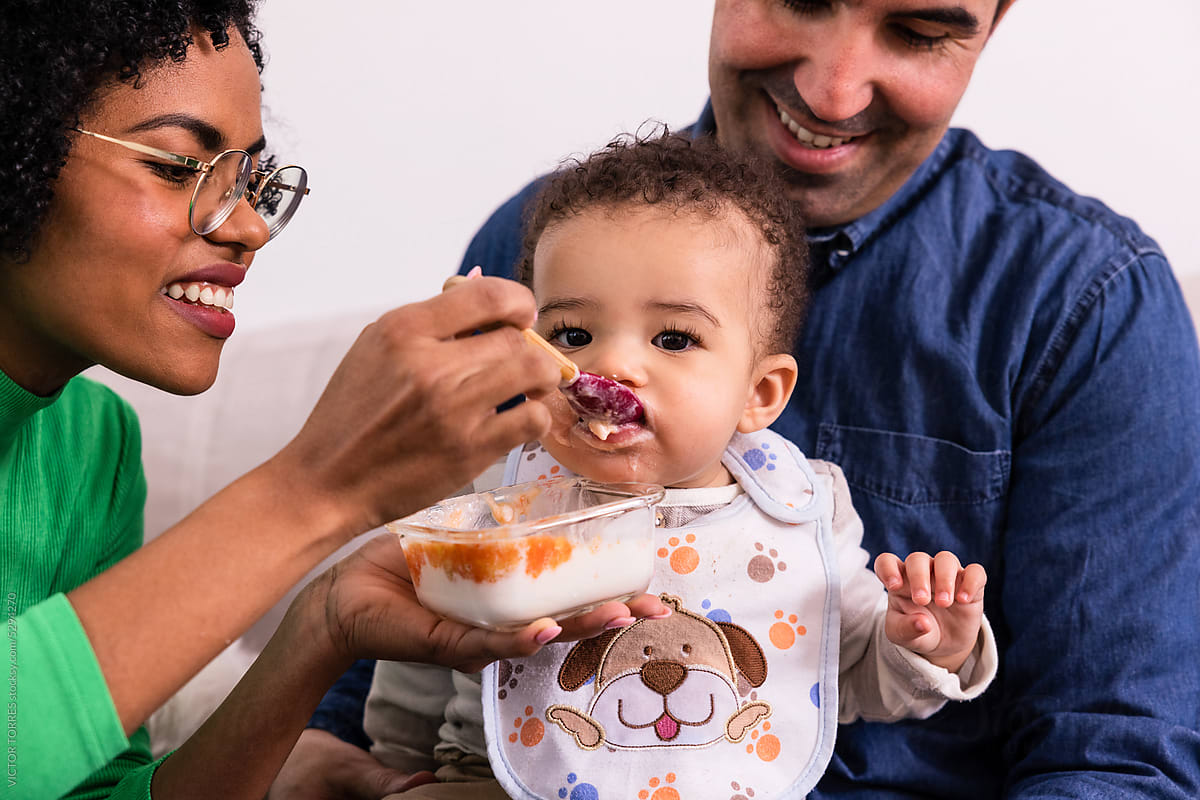 Cheerful black mother and father feeding little son with puree