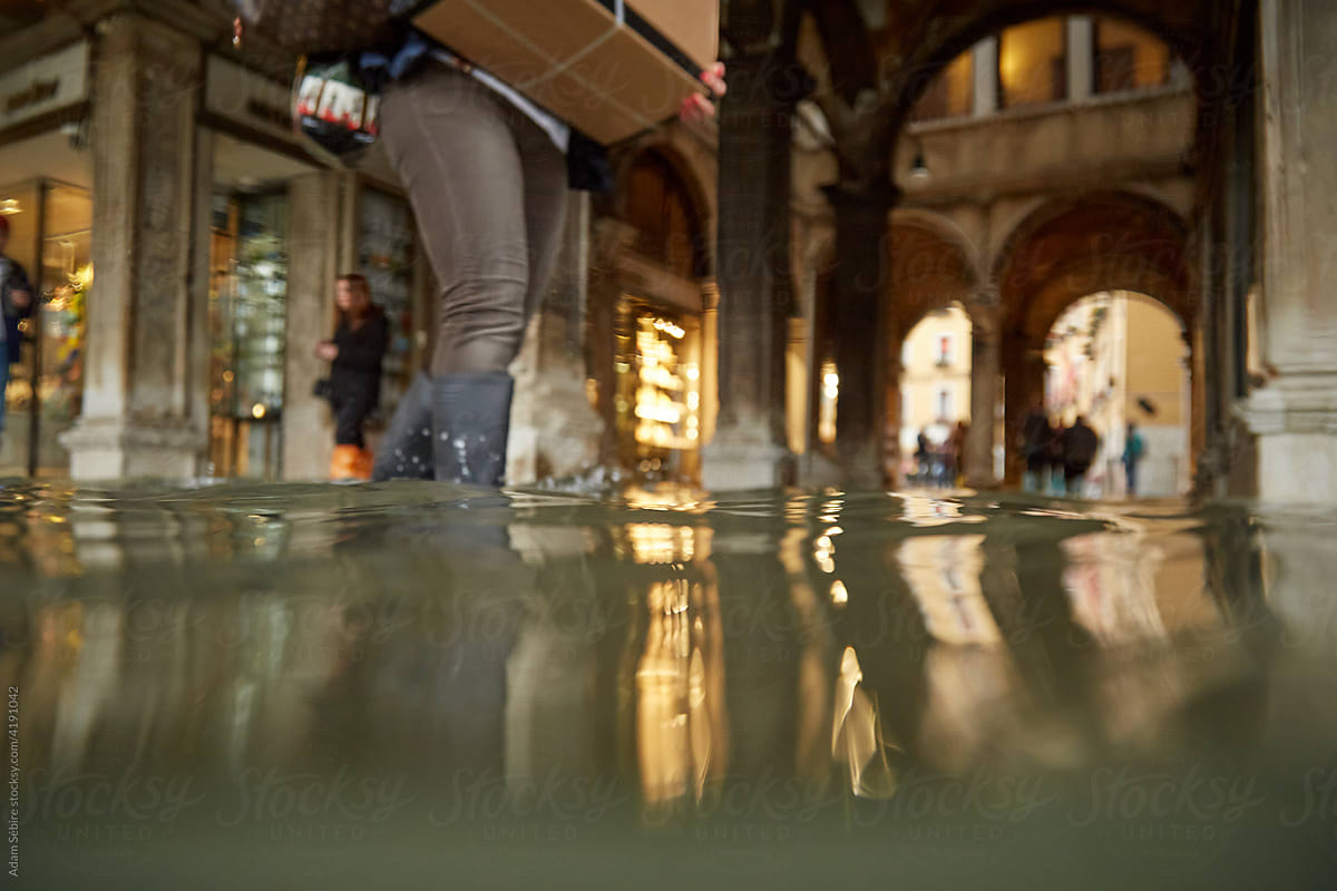 Venice floods, king tide, gumboot shopper wades with parcel