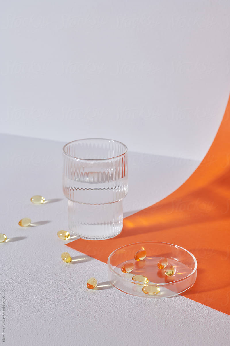Omega 3 fish liver oil capsules and glass of water on table.