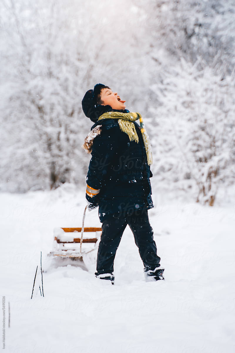 full body length boy child catching falling snowflakes in mouth