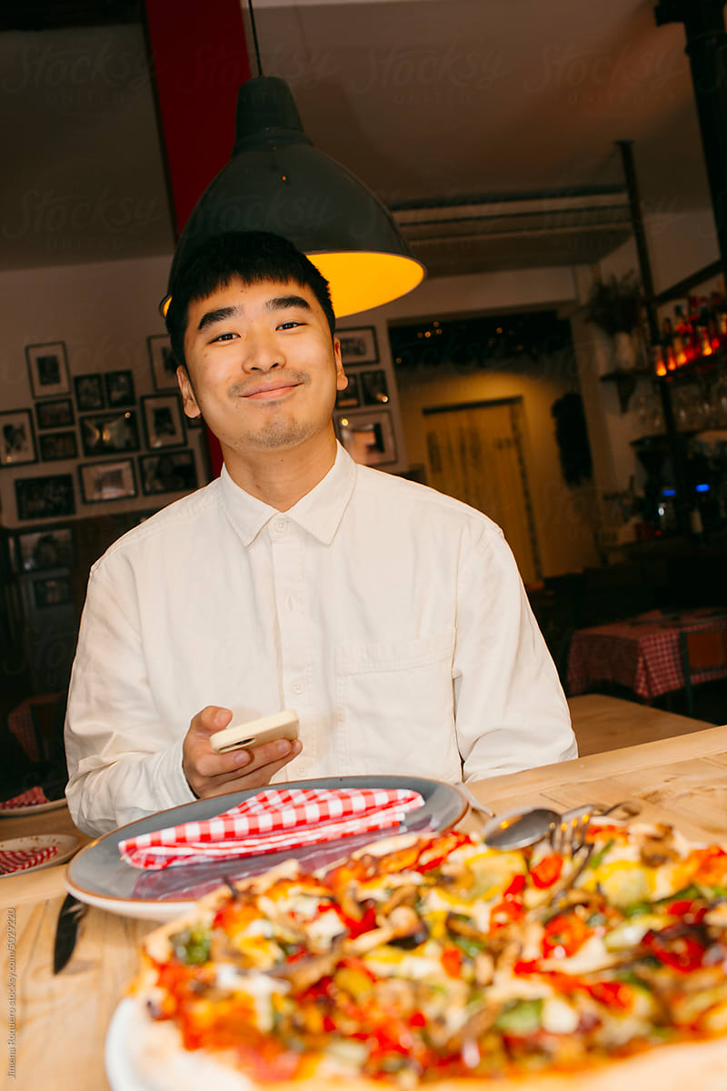 Happy young man eating pizza in restaurant looking at camera smiling