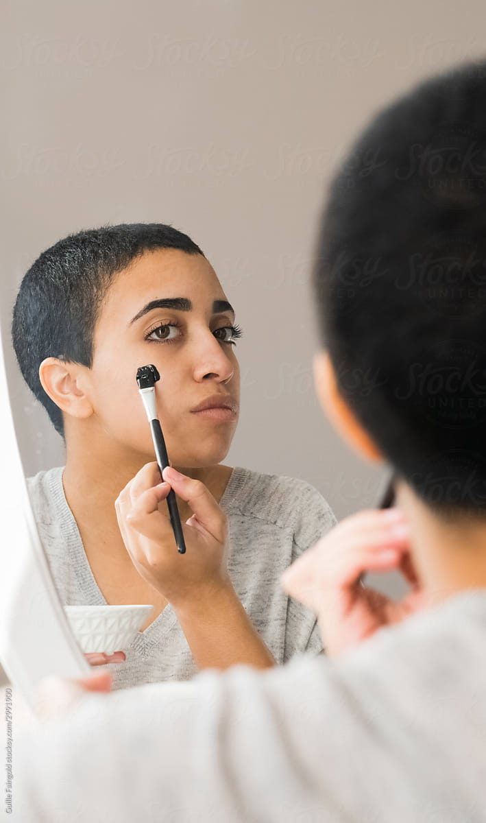 Girl applying facial mud mask in front of mirror