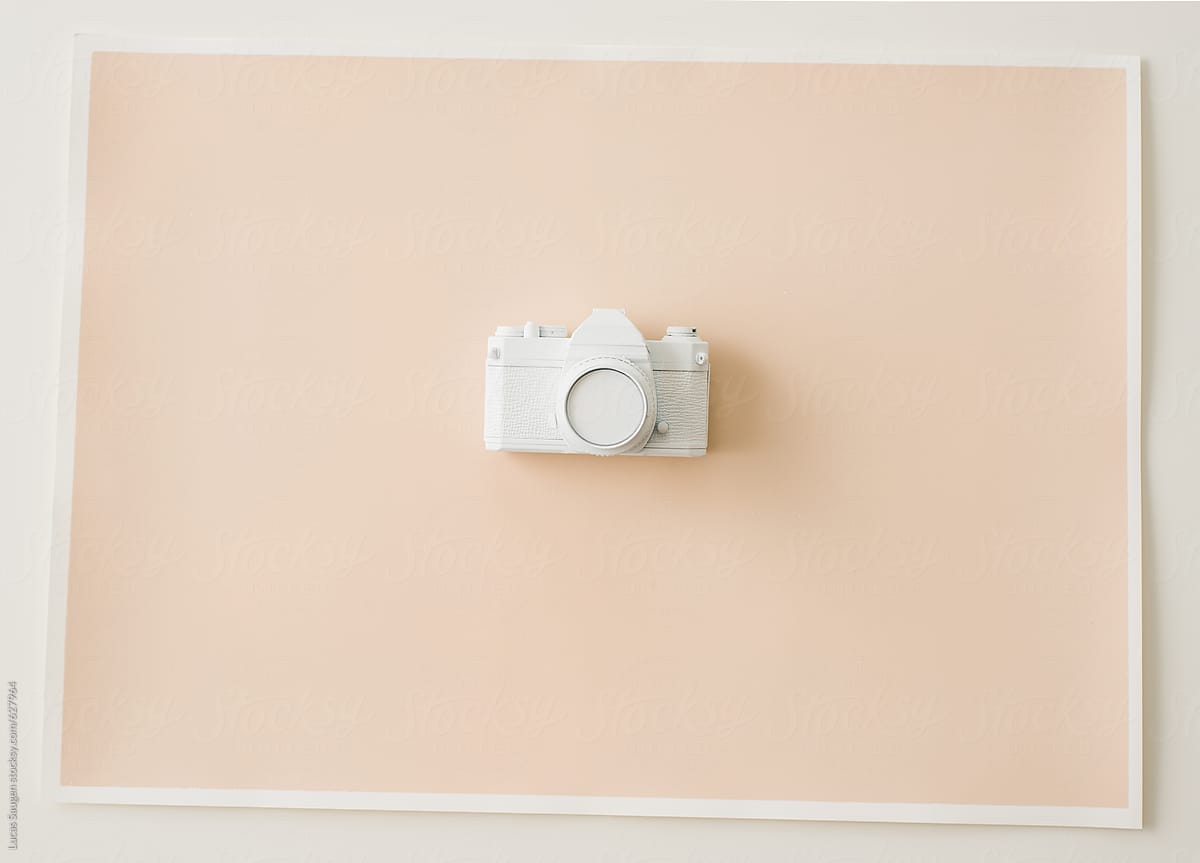 An old film camera painted white and place on a peach painted paper.
