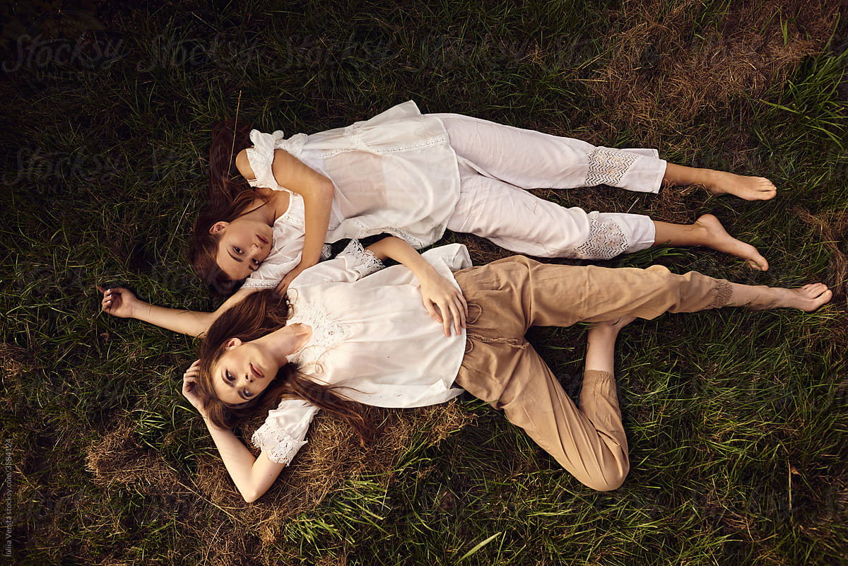 Top view of two female models in vintage clothes posing lying on the grass outdoors.