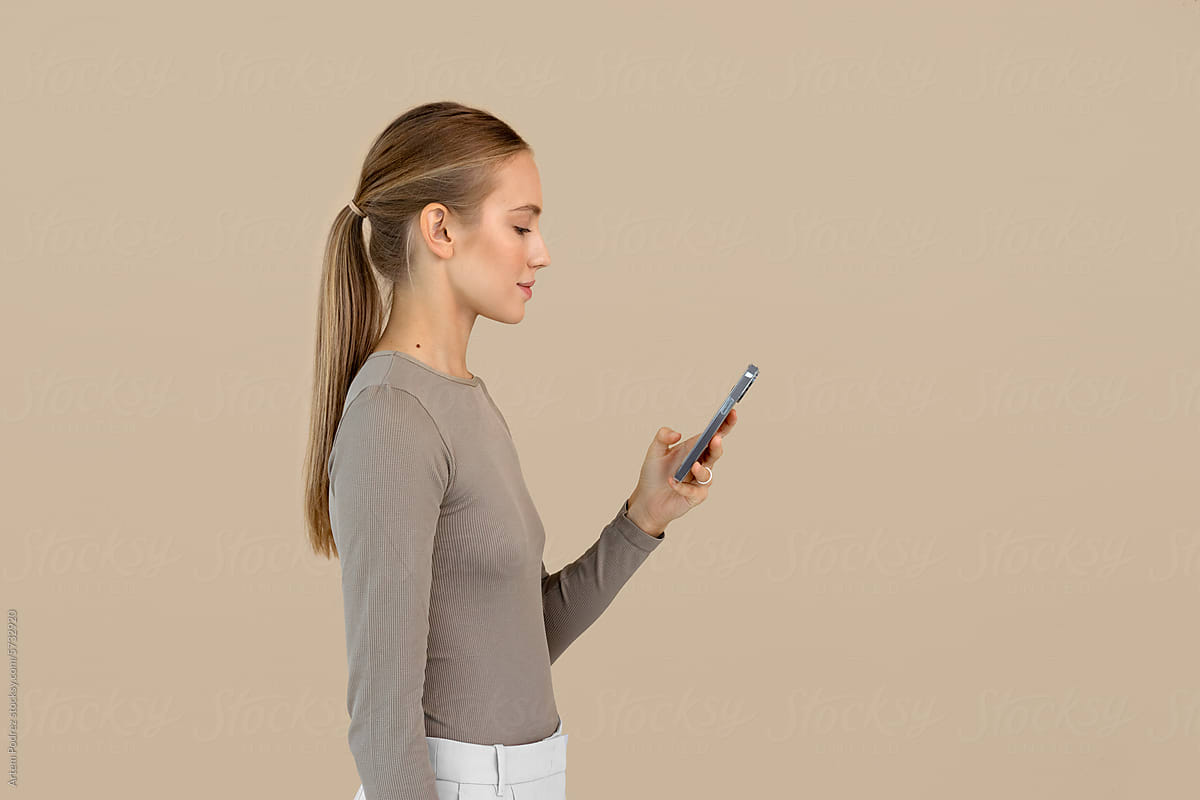 A woman uses a phone on a beige background