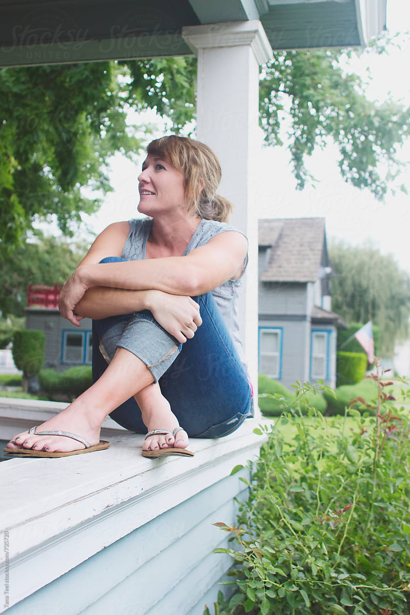 woman sits crossed leg on front porch rail