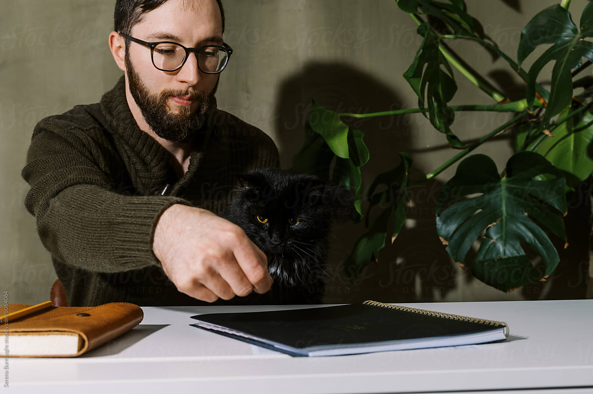 Man in his home office playing with his black cat