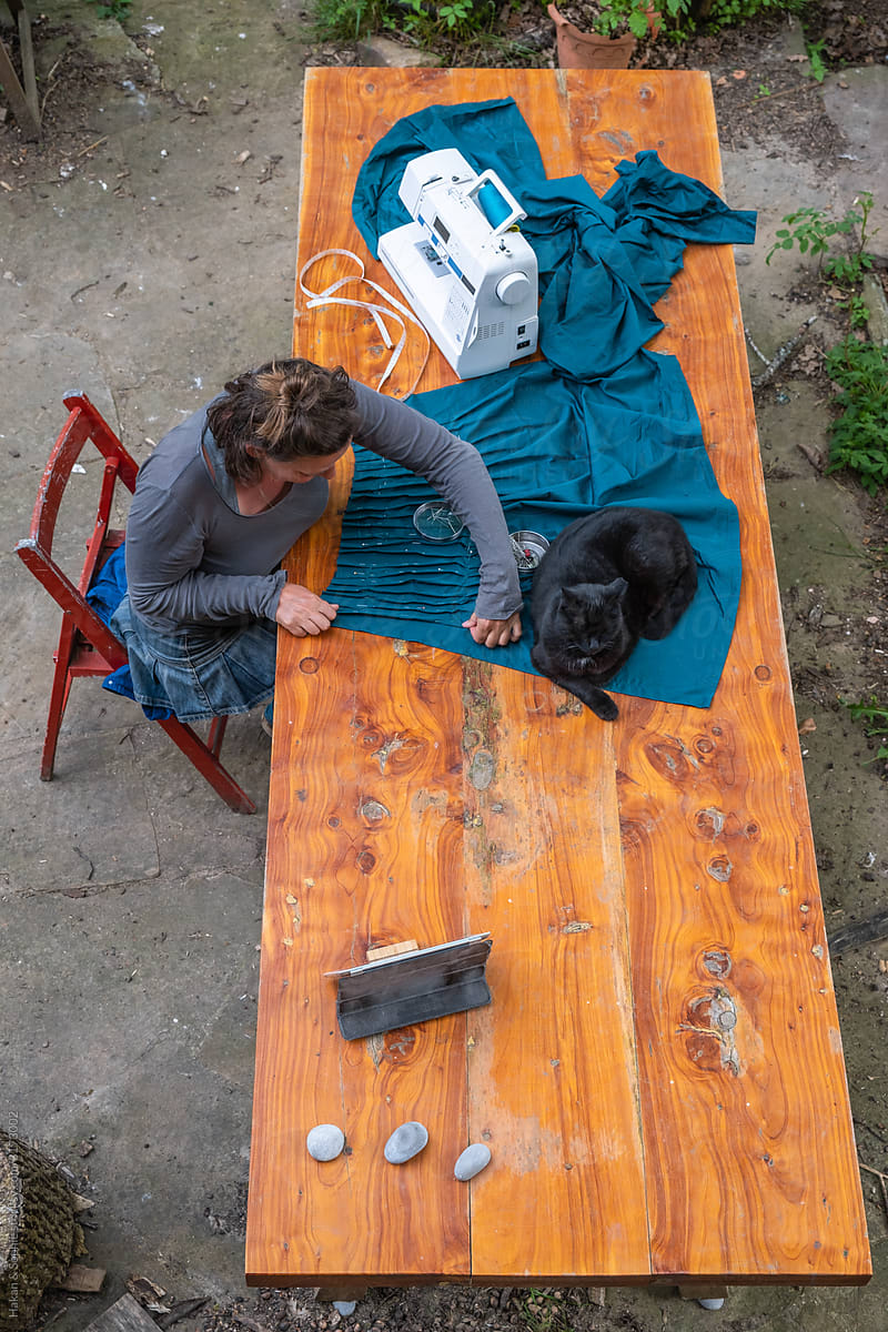 woman sewing outdoors with a cat