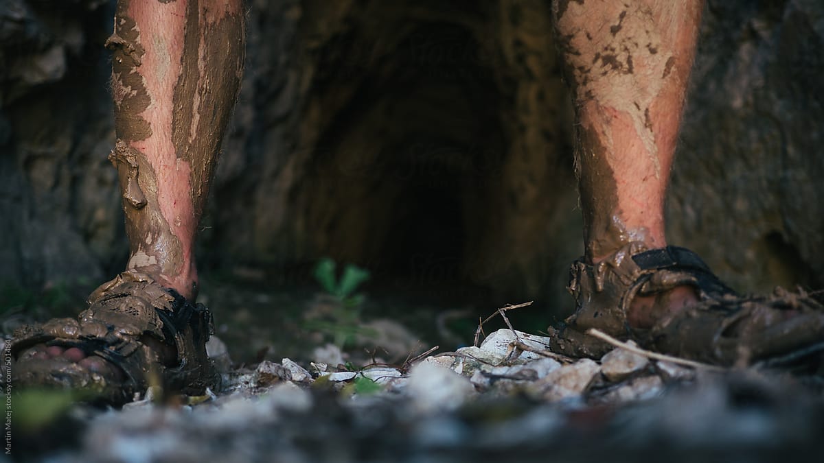 Feet in sandals dirty from mud with dark tunnel behind