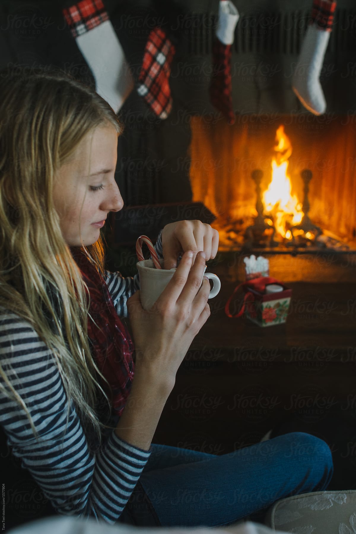 teenager holds cup of coco while sitting near fireplace during Christmas holiday