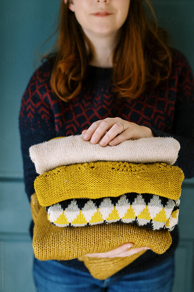 Happy smiling woman holding stack of handmade knit sweaters