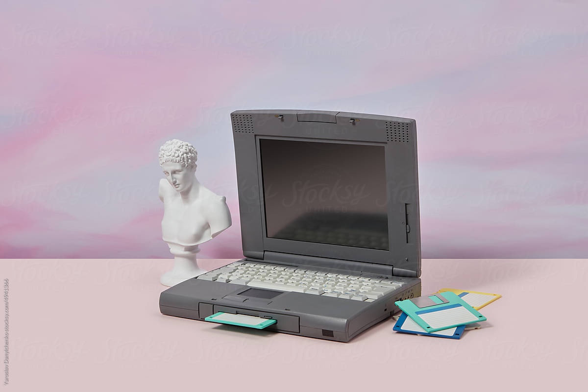 Old laptop with antique statue and floppy disks.
