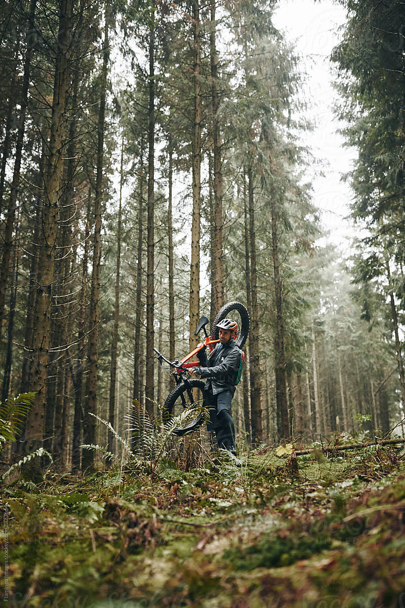 Lone mountain biker carrying his bike in a misty forest
