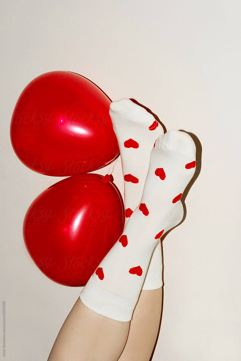 Legs lie upside down against a wall with red balloons