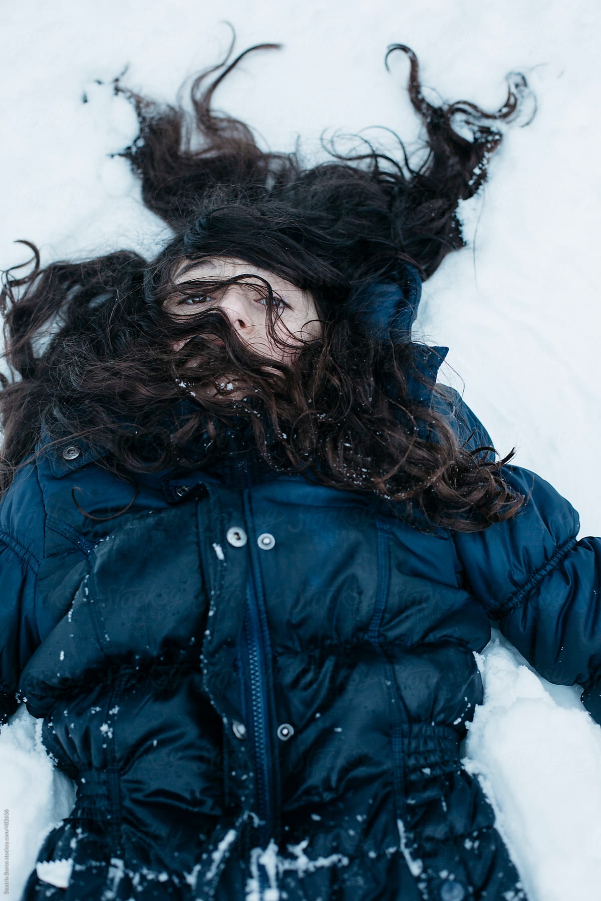 Tired girl in coat laying on the snow, her hair is all over her face