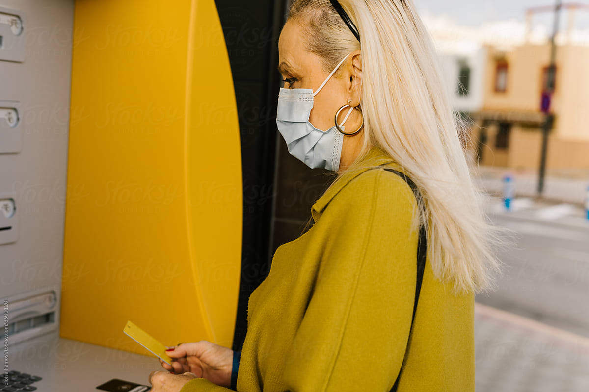 senior woman with protective mask using ATM