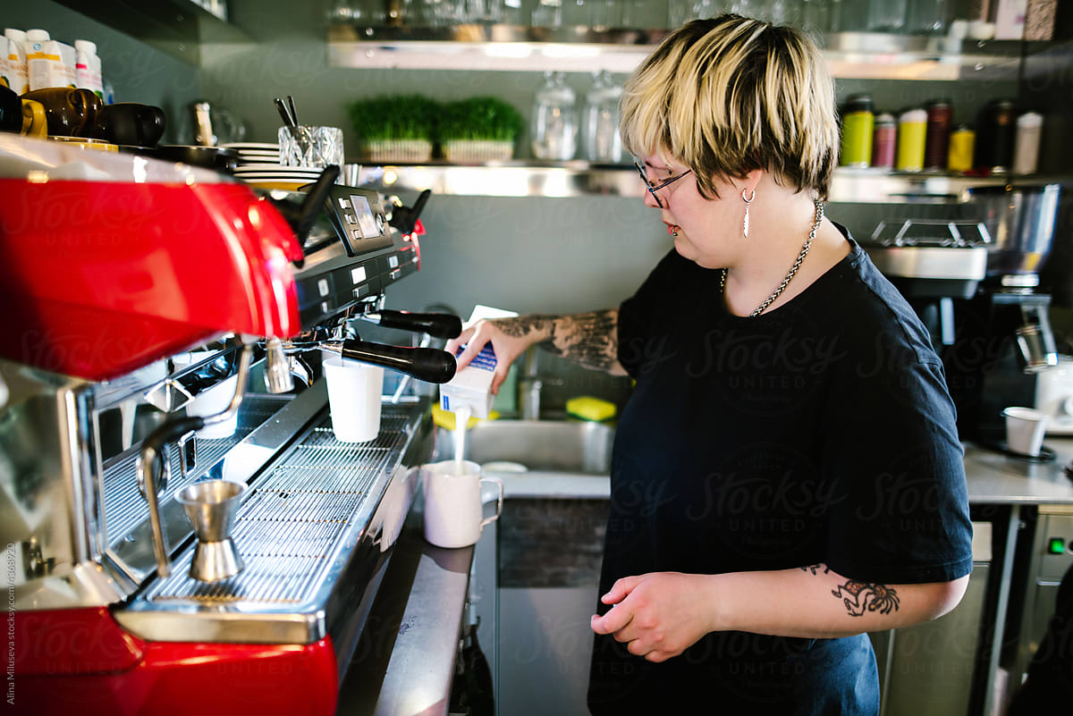 Woman barista pouring milk into a pitcher