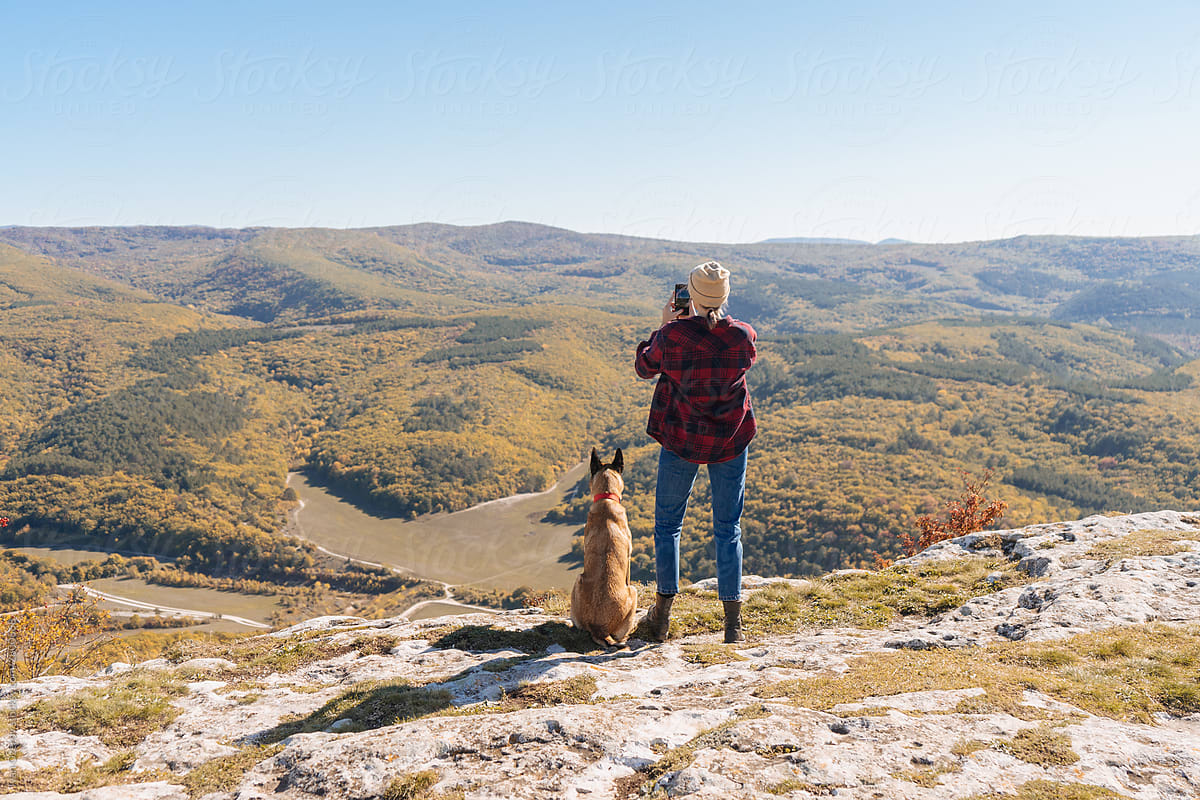 A girl photographs a wonderful landscape on the phone while her dog sits nearby