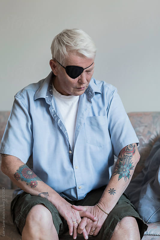 Portrait of elderly woman with eye patch looking at her tattoos