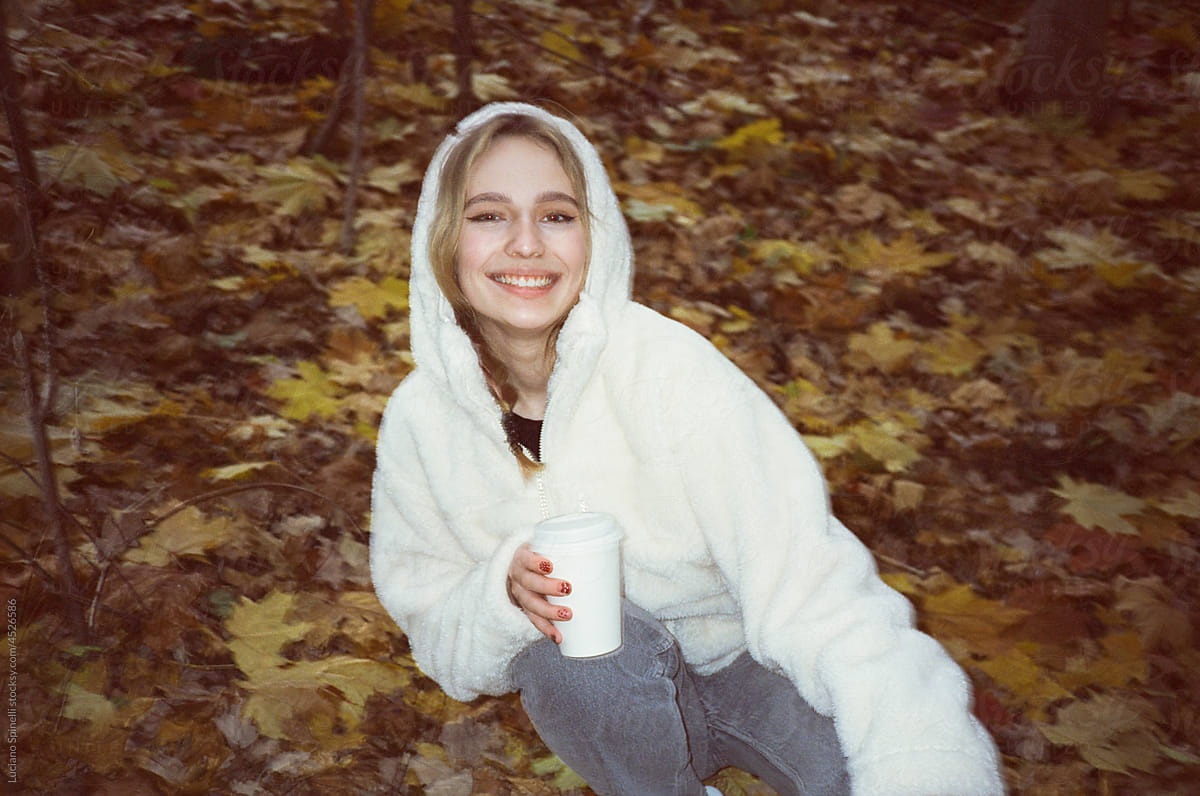 Girl smiling and holding a white cup during a grey autumn afternoon