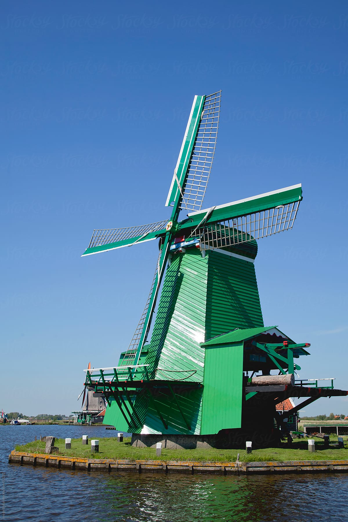 A classic green Dutch windmill surrounded by water under a clear blue sky