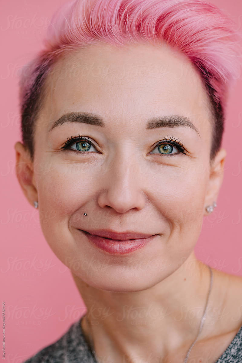 Closeup portrait of smiling woman with short pink hait posing by pink backdrop