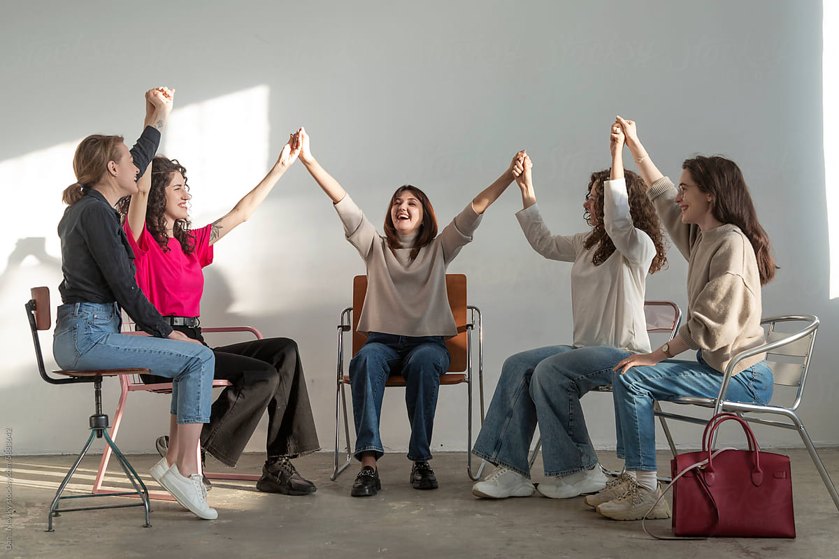 Cheerful women holding hands up while sitting together in meeting