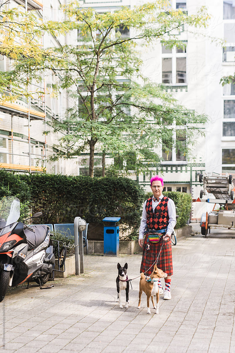 Man with pink hair in a funky kilt walking basenji dogs