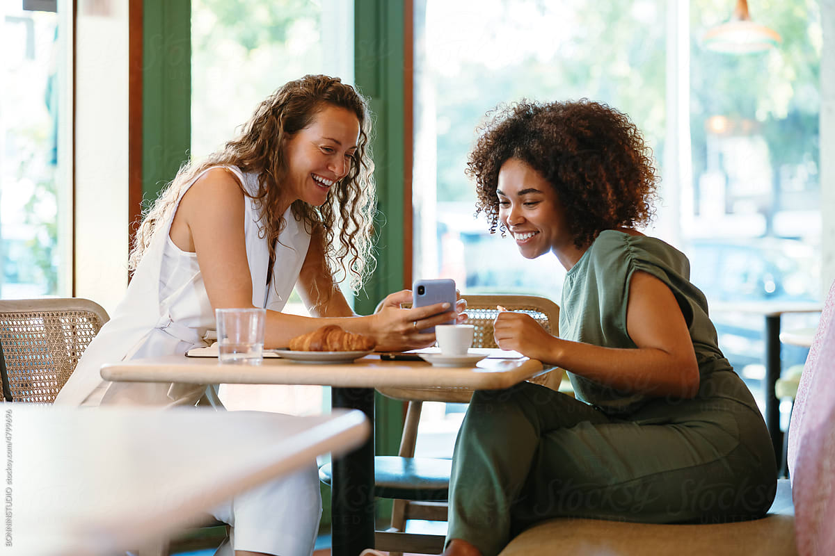 Diverse girlfriends using smartphone in cafe