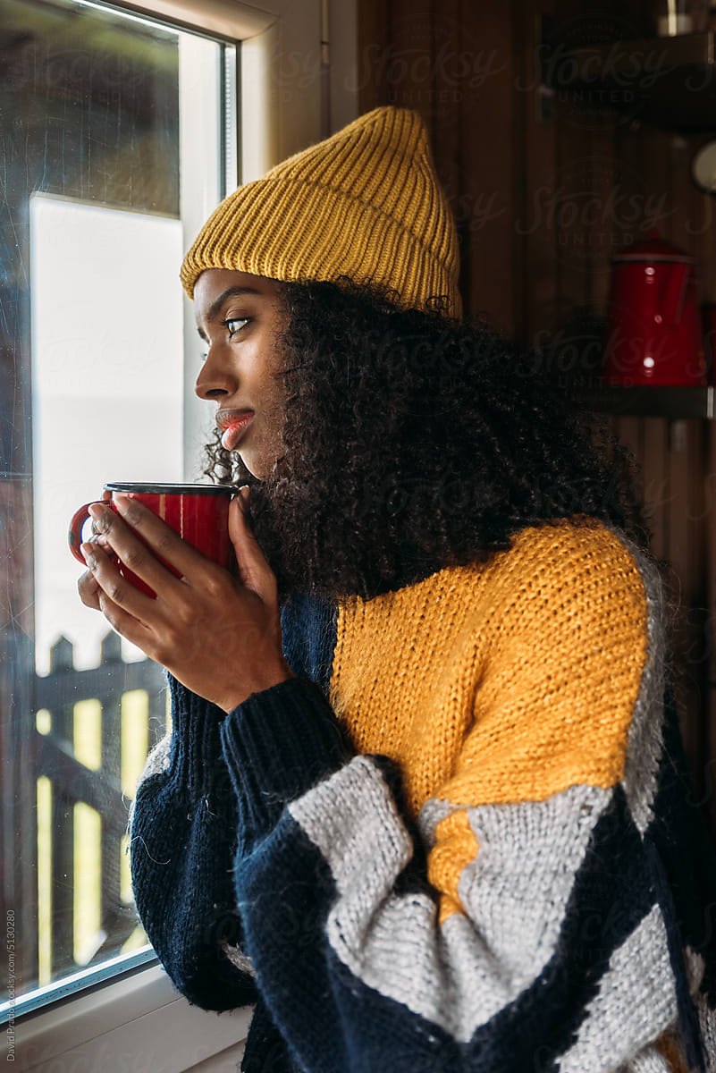 Black woman enjoying hot drink near window