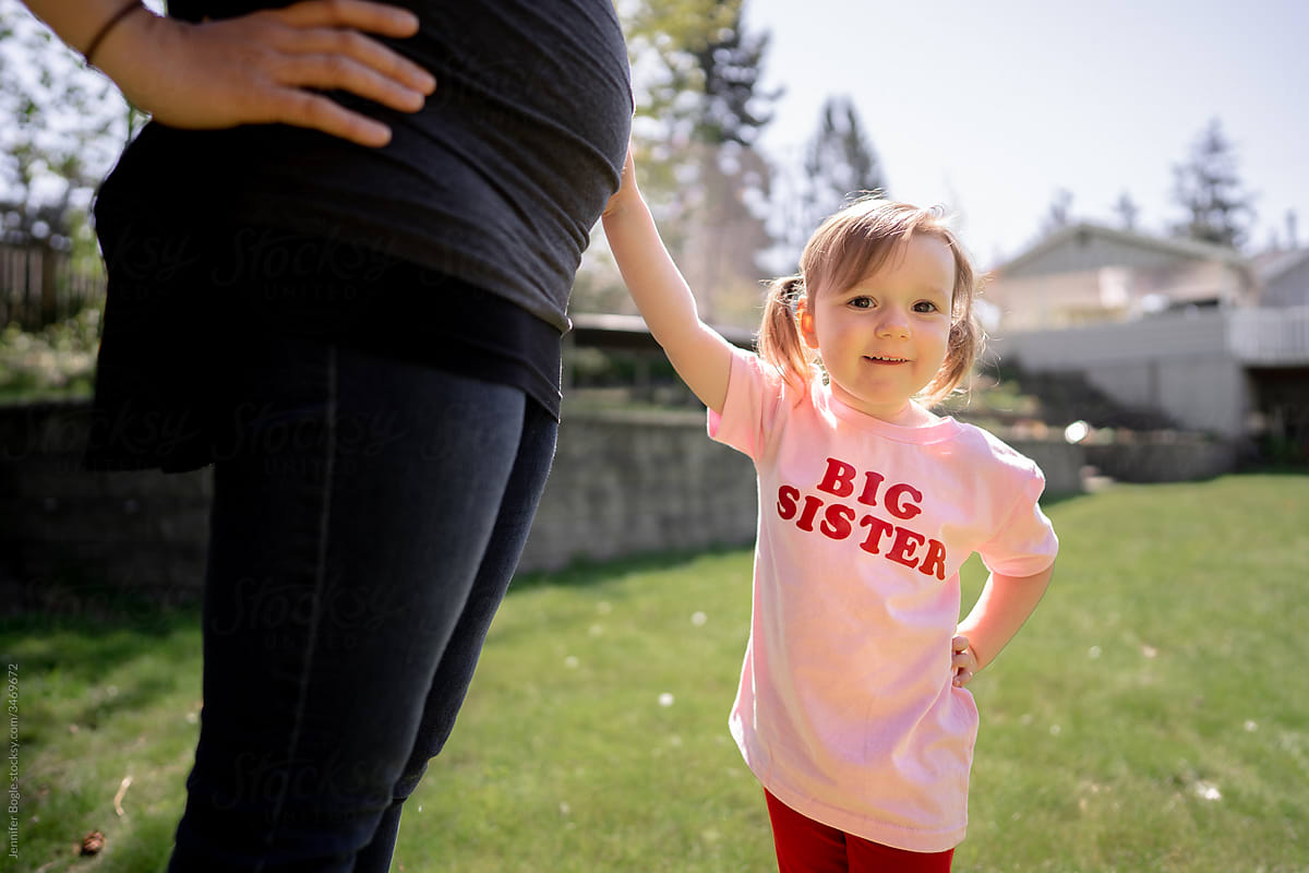 Cute toddler stands with hand on mom\'s pregnant belly