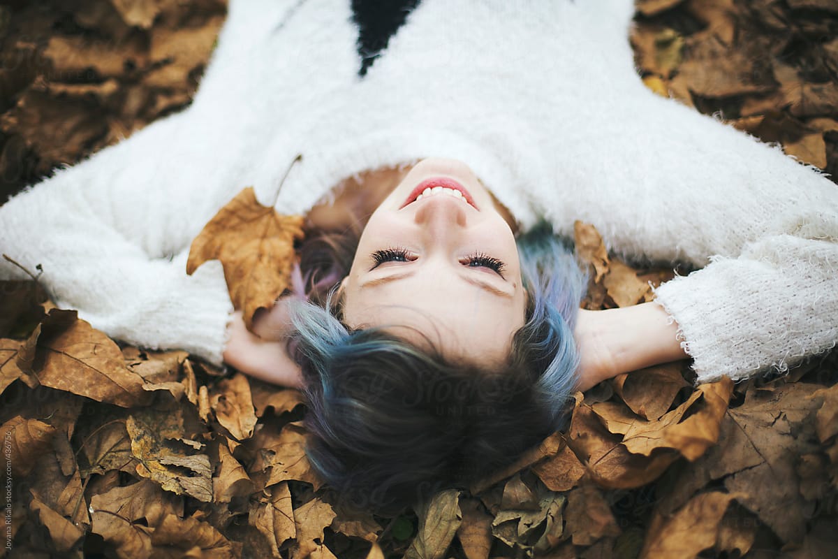 Portrait Of A Beautiful Young Woman Lying Down In Autumn Leaves And Smiling By Stocksy