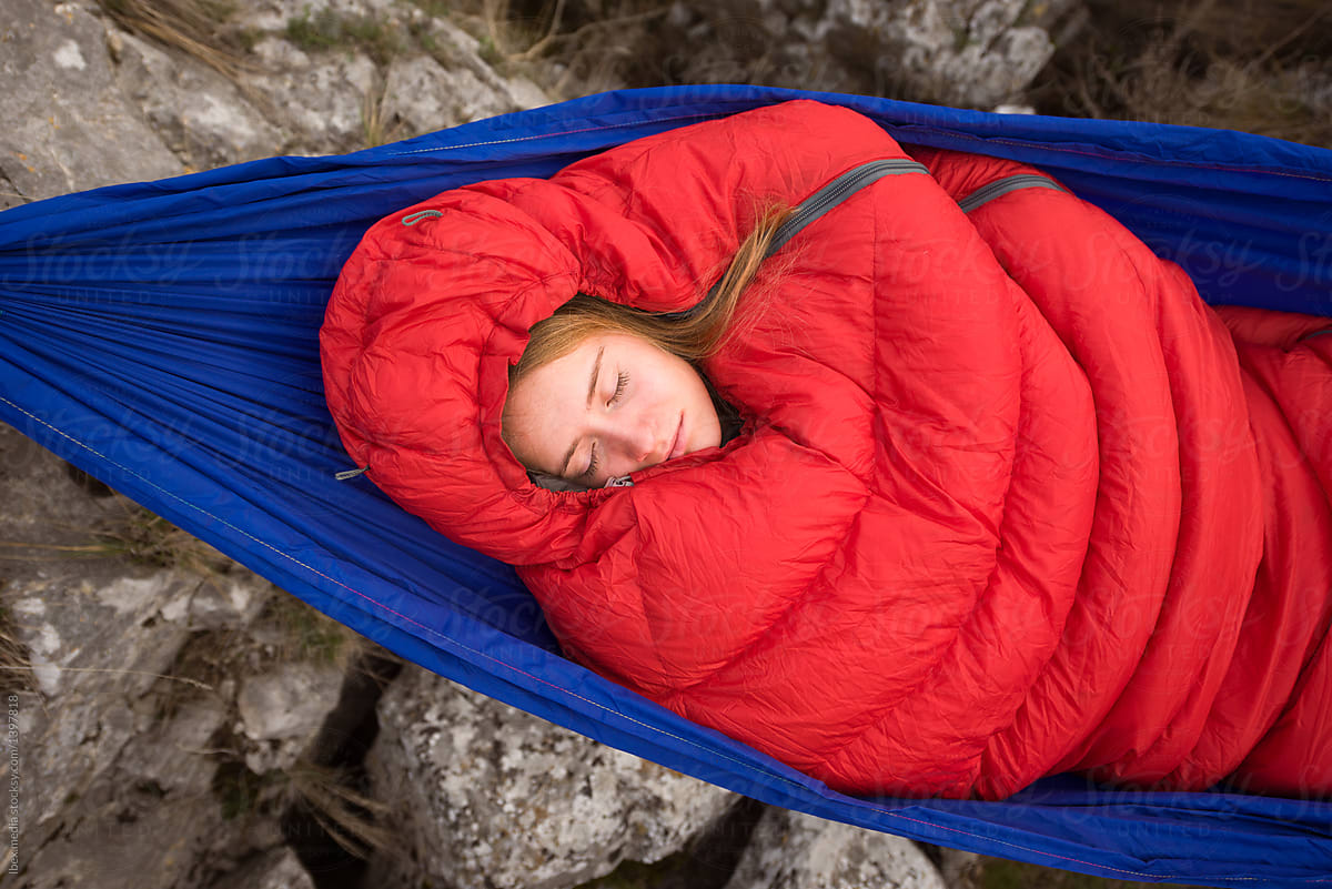 Woman coverd with red sleeping bag resting in hammock