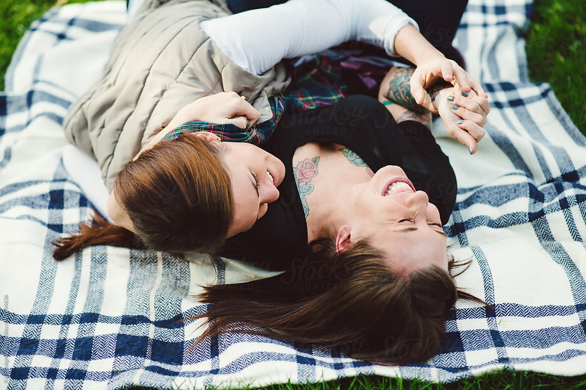 Lesbian couple embracing on a blanket in the park.