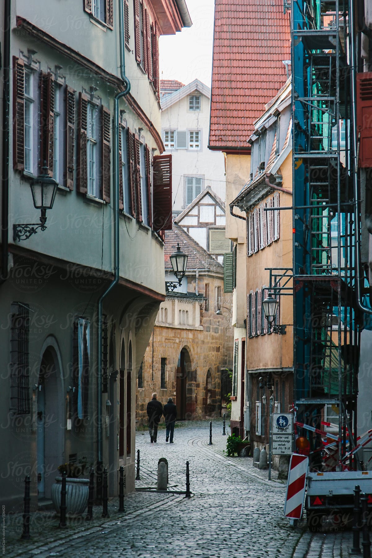 Two figures walk down narrow cobblestone German street