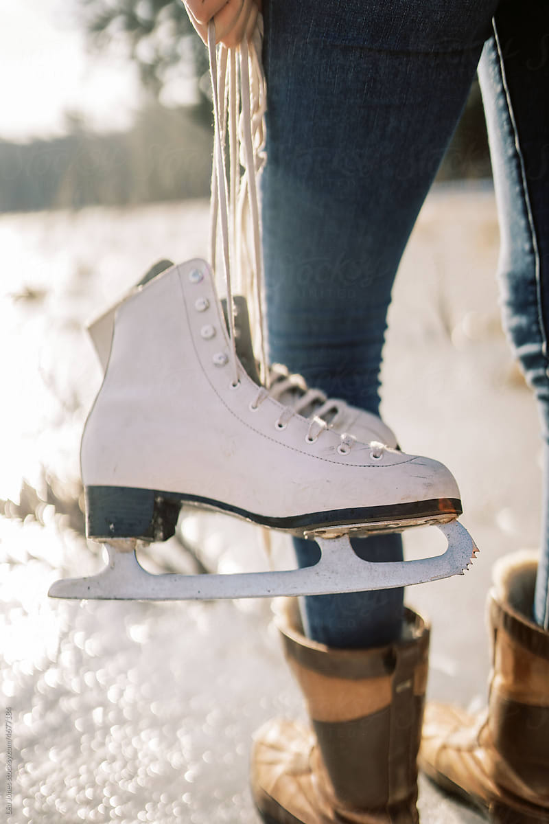 close up of skates held by a woman by a lake