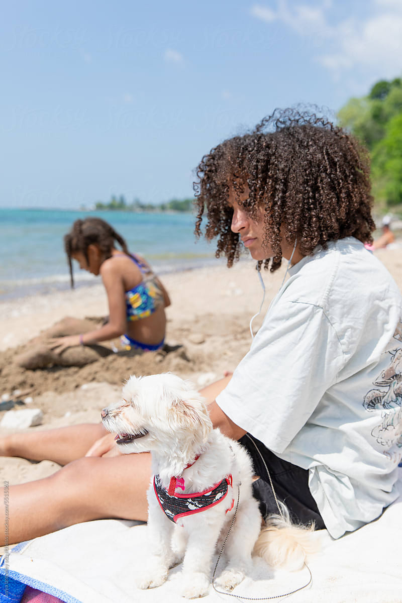 Teen with curly hair sitting with her dog while on the beach
