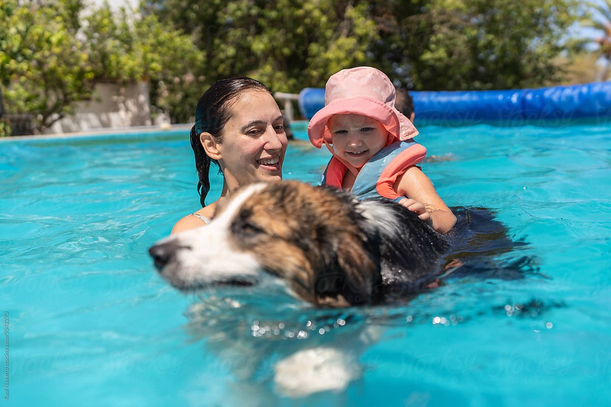 mother with her baby swimming in the pool with her dog