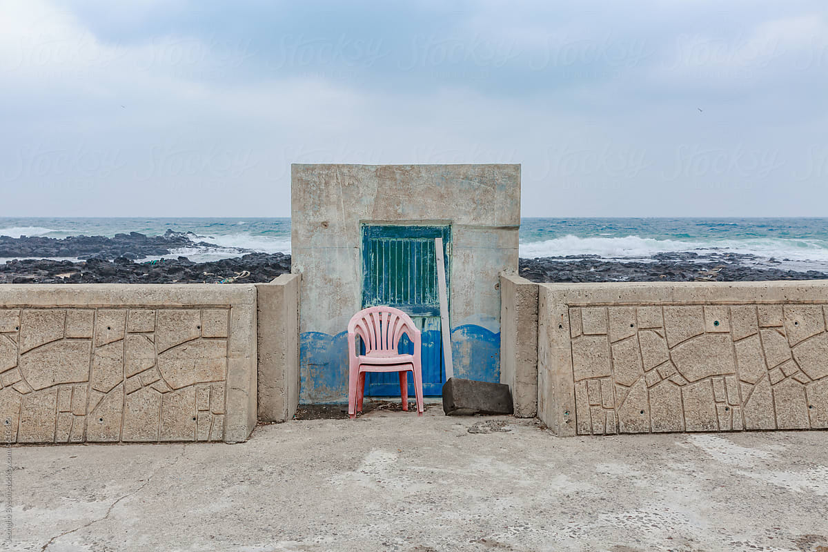 A chair in front of the blue door of a small waterfront building.