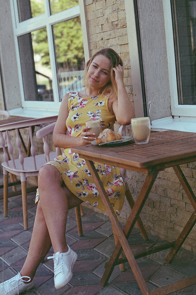A blond girl sits at the street cafe in the sundress