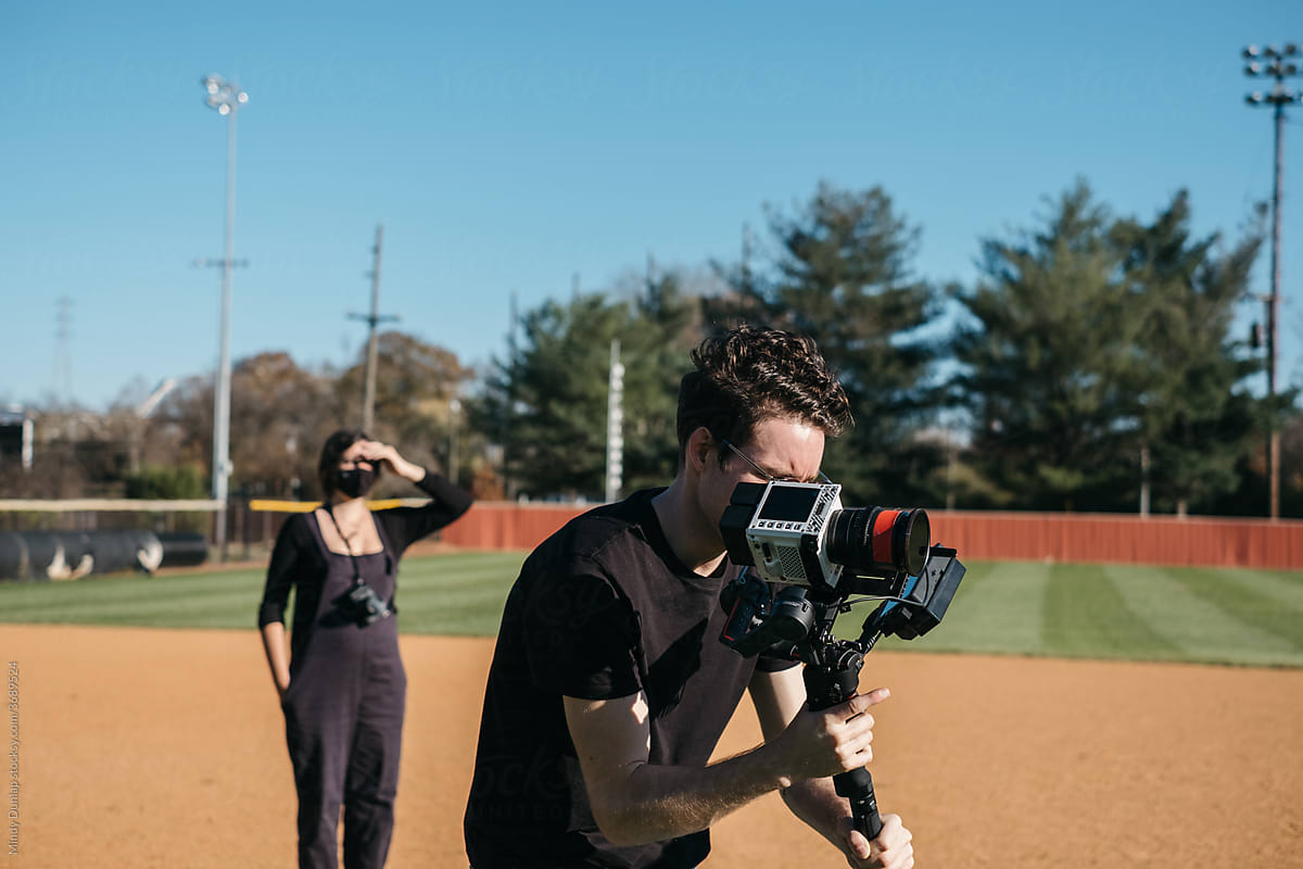A young cinematographer filming on a baseball field