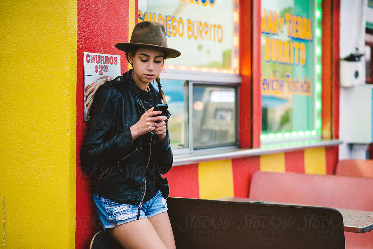 Trendy teenage girl on her smartphone outside a taco shop at night