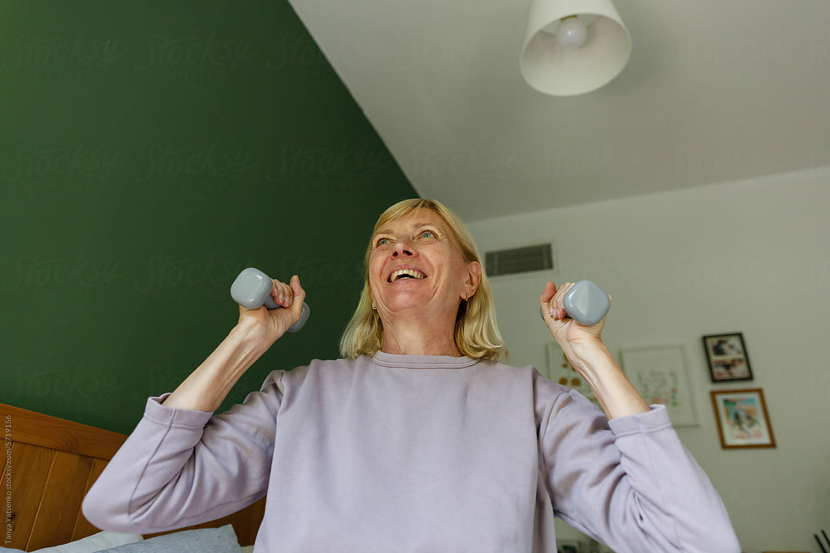 Smiling Senior Woman Exercising With Dumbbells in bed