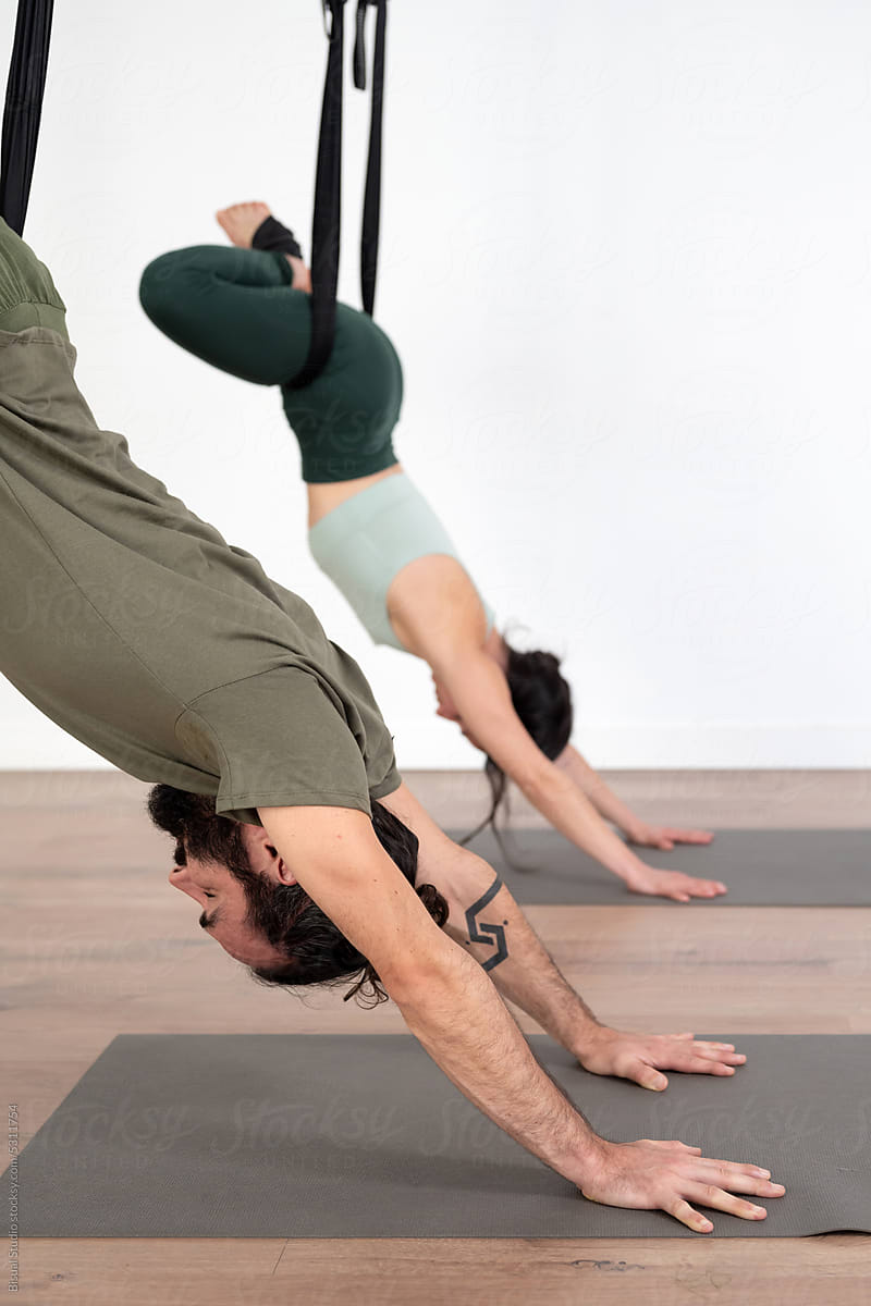 Woman and man doing aerial yoga exercise in gym