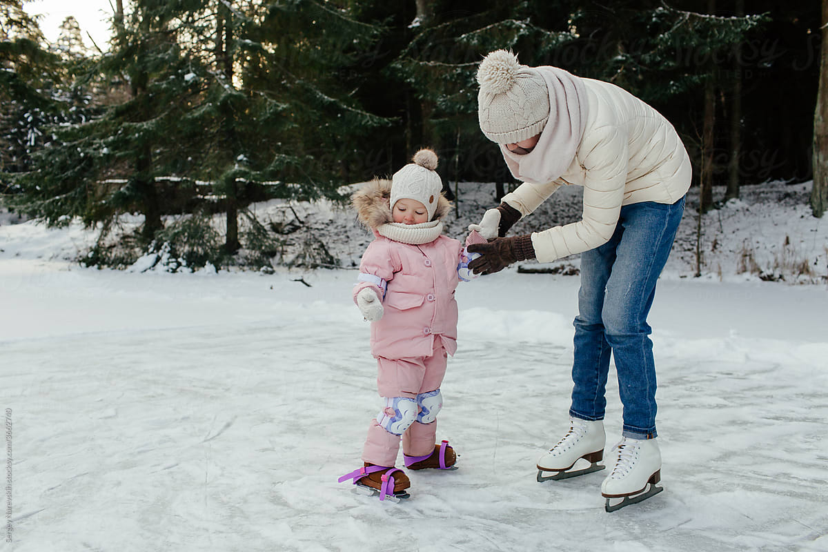 Happy little child with mom preparing skating on ice in forest